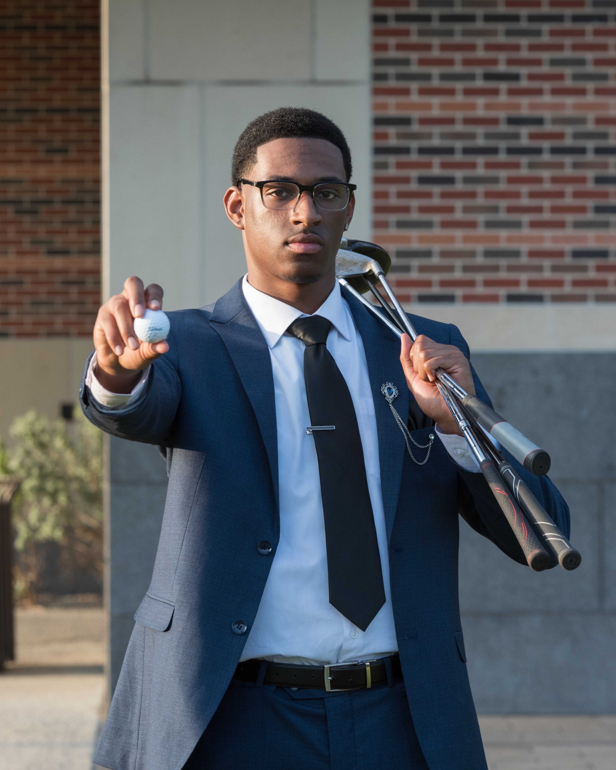 African American male student at PVAMU taking photos with a golf ball and golf clubs in front of the Prairie View A&M School of Business