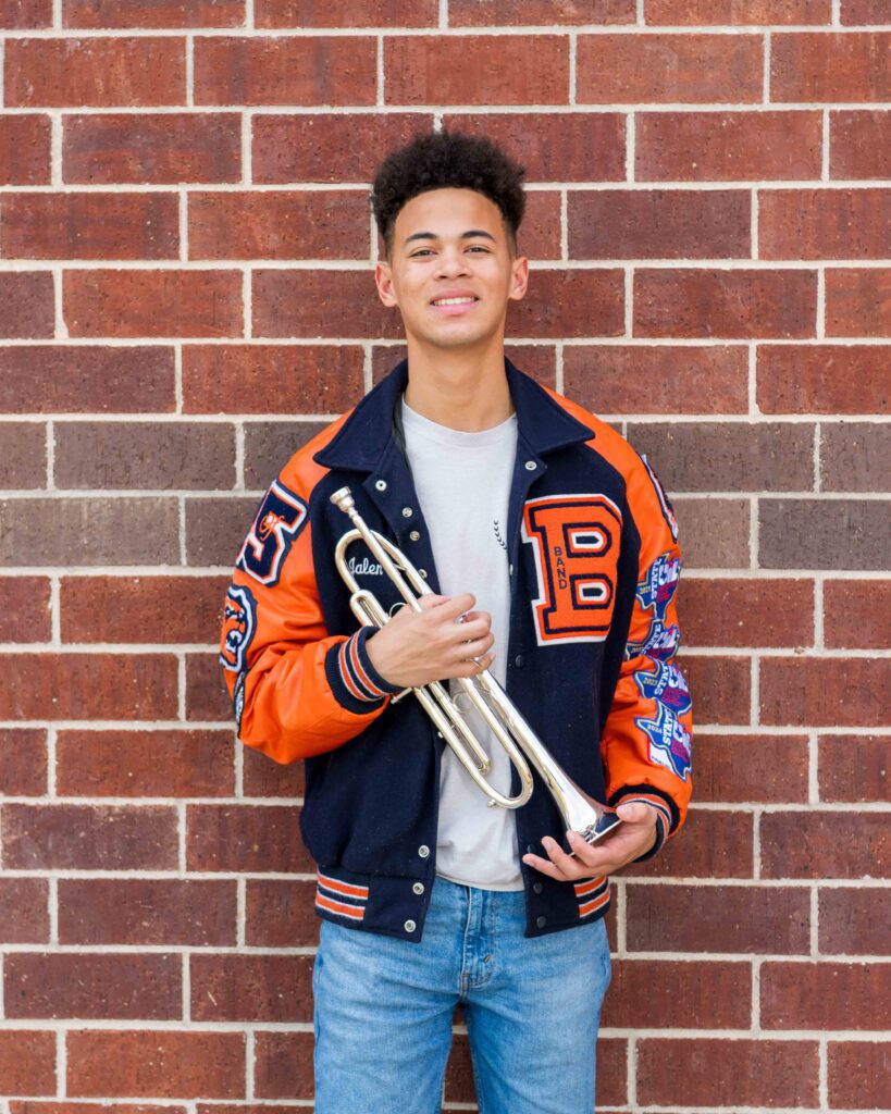 Cypress senior photo of Bridgeland band member holding trumpet with Bridgeland letterman jacket.