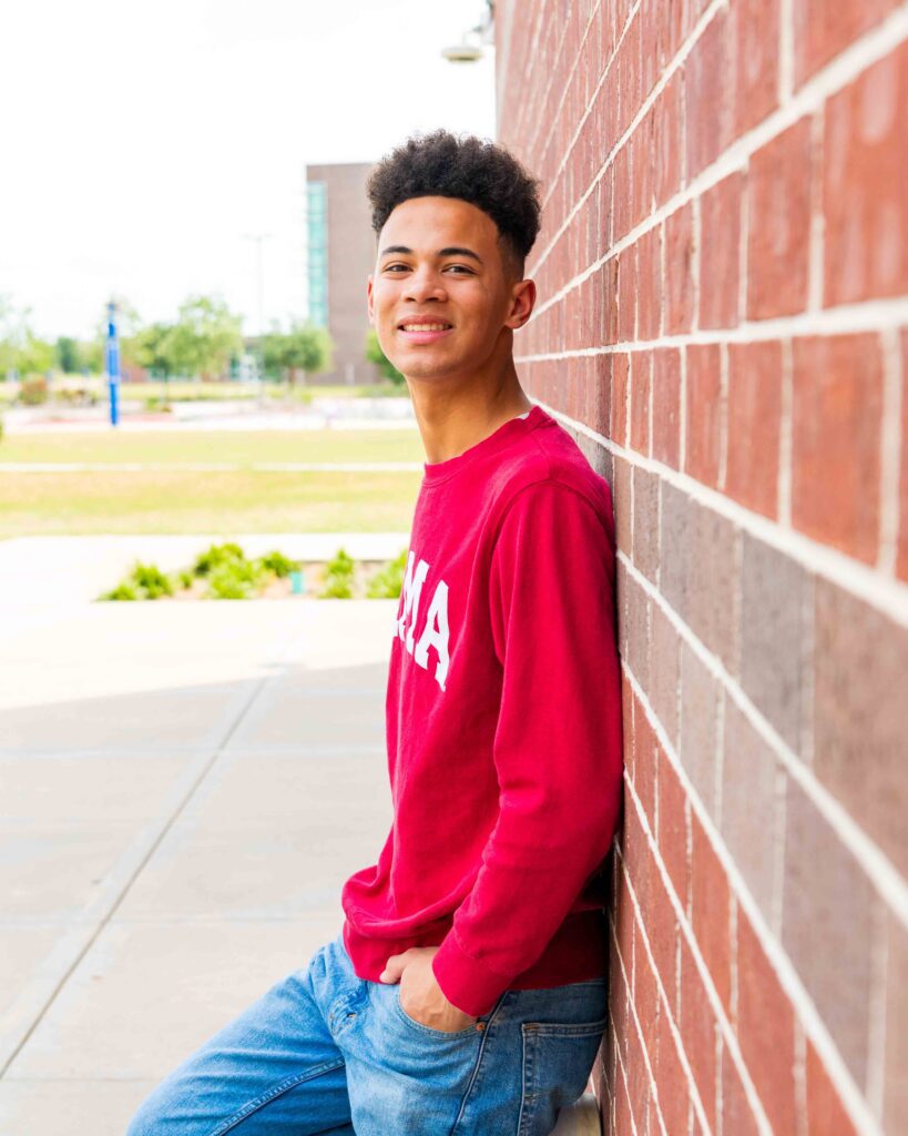 Cypress senior portraits with Jalen Francis in red Bama sweatshirt at Bridgeland High brick wall