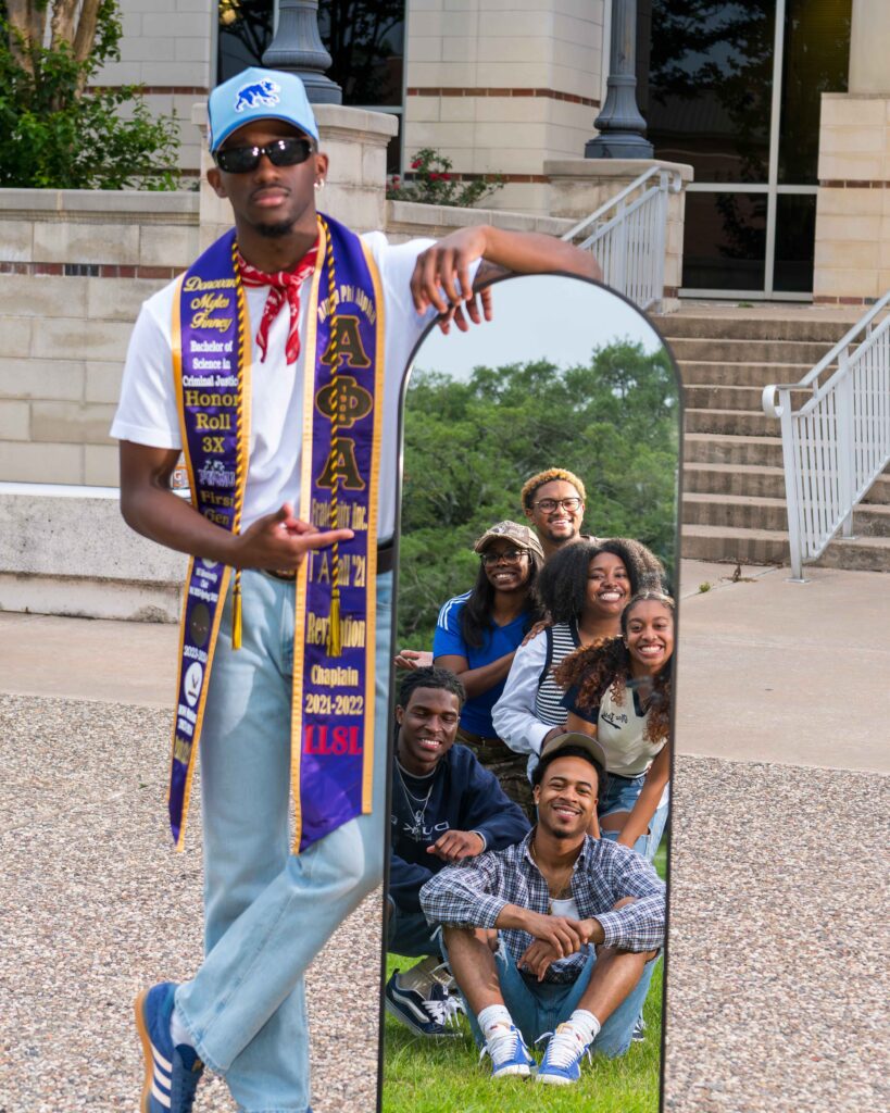 PVAMU grad Donovan 'Donny' Finney in Alpha Phi Alpha stole poses by a mirror reflecting his friends on the Prairie View A&M campus.